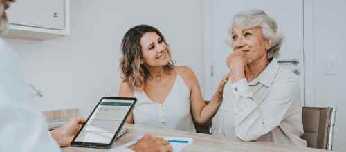 Foto de duas mulheres sorrindo a frente de um profissional no consultorio com tablete na mão, indicando que está consultando o sistema Darwin