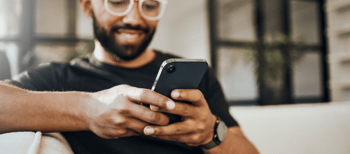 Homem afro-descendente usando oculos e camiseta preta, olhando o celular sorrindo, indicando estar consultando o sistema darwin